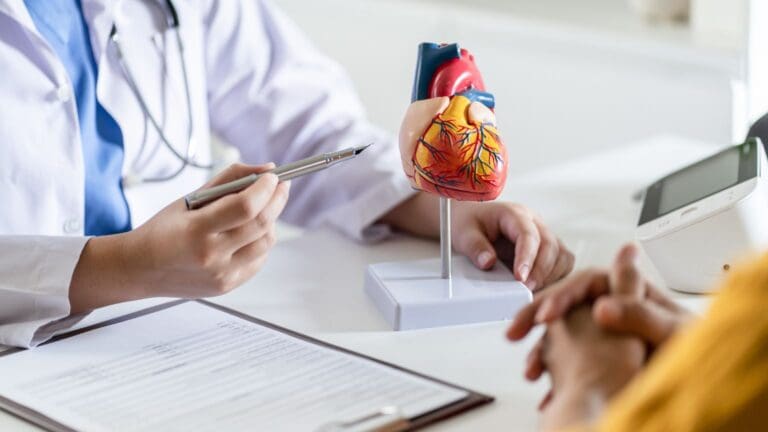 Consulta médica para la prevención de enfermedades cardíacas, con corazón rojo y estetoscopio sobre mesa blanca, simbolizando la salud cardiovascular.