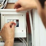 Persona revisando un cuadro eléctrico en una vivienda para asegurar la protección de la instalación ante fallos y prevenir sobrecargas eléctricas.