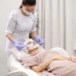 Paciente recibiendo tratamiento facial en clínica estética bajo supervisión médica en un entorno seguro y profesional.