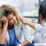 Mujer visiblemente agotada emocionalmente recibiendo apoyo de otra mujer, posible terapeuta, en un entorno que representa la atención integral de un centro médico.