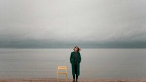 Mujer de pie frente al mar en un entorno silencioso, representando la conexión entre reflexión, calma y salud mental.
