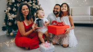 Familia sonriendo junto al árbol de Navidad mientras intercambian regalos para niños