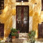 Fachada antigua de vivienda con puertas y contraventanas de madera, plantas y detalles originales ideales para restauración en una reforma integral.