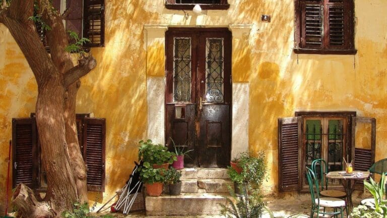 Fachada antigua de vivienda con puertas y contraventanas de madera, plantas y detalles originales ideales para restauración en una reforma integral.