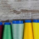 Bobinas de hilos de coser de distintos colores y grosores organizadas sobre una mesa, mostrando opciones para costura profesional y creativa.