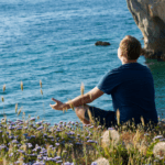 Persona meditando frente al mar en un entorno natural y tranquilo