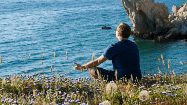 Persona meditando frente al mar en un entorno natural y tranquilo