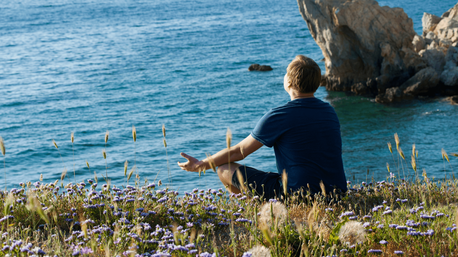 Persona meditando frente al mar en un entorno natural y tranquilo