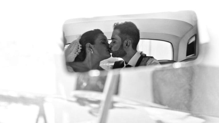 Reflejo en blanco y negro de unos novios besándose en el coche el día de su boda, capturado como parte de unas fotos de bodas con estilo artístico y romántico.
