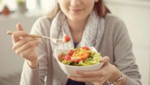 Mujer observando un plato de comida con expresión reflexiva, representando cómo una nutricionista puede ayudar a entender el malestar a pesar de comer bien.