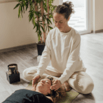 Terapeuta realizando una sesión de reiki a una mujer tumbada en un espacio tranquilo con ambiente relajante y luz natural.