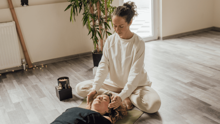 Terapeuta realizando una sesión de reiki a una mujer tumbada en un espacio tranquilo con ambiente relajante y luz natural.