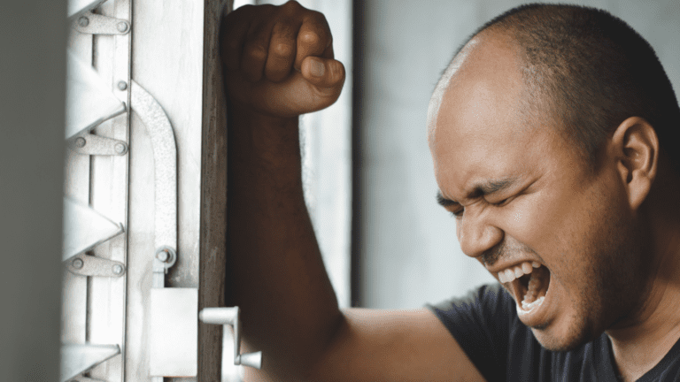 Hombre gritando con angustia apoyado en una puerta metálica, expresión de estrés emocional o ansiedad intensa