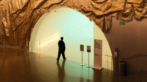 Persona entrando en una galería de arte contemporáneo con entrada futurista y decoración textil dorada en el techo.