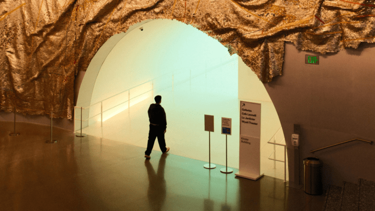 Persona entrando en una galería de arte contemporáneo con entrada futurista y decoración textil dorada en el techo.