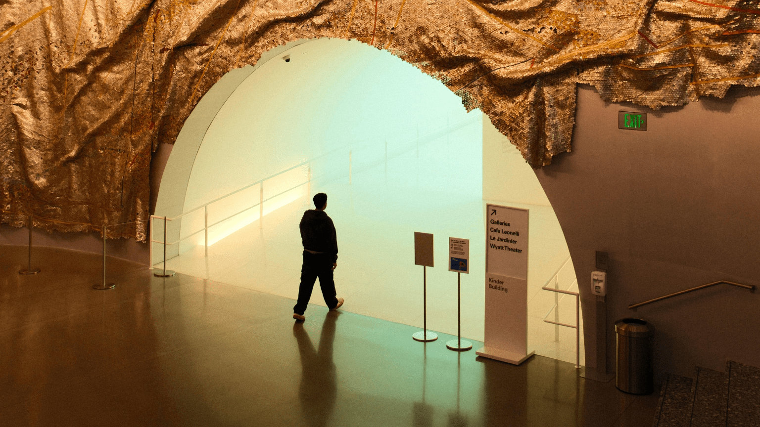 Persona entrando en una galería de arte contemporáneo con entrada futurista y decoración textil dorada en el techo.