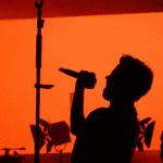 Cantante proyectando la voz en escenario con fondo rojo durante una actuación en Valencia.