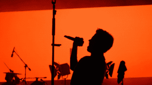 Cantante proyectando la voz en escenario con fondo rojo durante una actuación en Valencia.