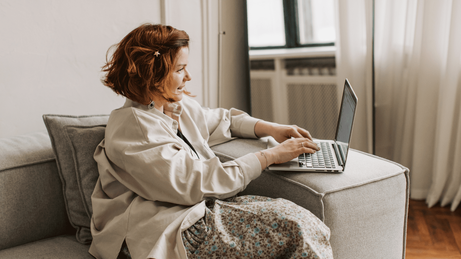 Mujer sonriente utilizando un portátil desde el sofá mientras realiza formación online sobre hábitos saludables desde casa.