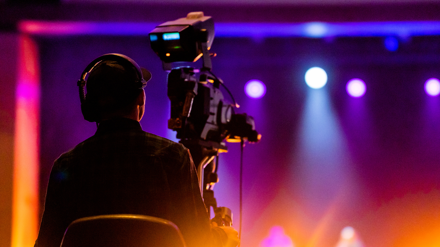 Técnico de cámara grabando en un set con iluminación de colores durante una producción audiovisual profesional.