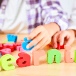 Niños aprendiendo inglés de forma divertida con letras de colores sobre una mesa durante una actividad educativa infantil.