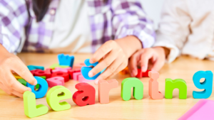 Niños aprendiendo inglés de forma divertida con letras de colores sobre una mesa durante una actividad educativa infantil.