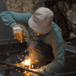 Soldador profesional trabajando en la fabricación de estructuras metálicas con técnicas de soldadura por arco en taller industrial.