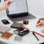 Selección de materiales y acabados para proyecto arquitectónico sobre mesa de trabajo, con planos y muestras visibles.
