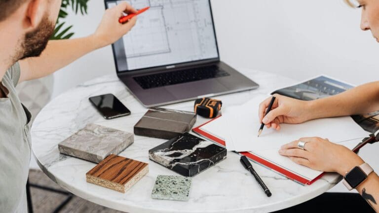 Selección de materiales y acabados para proyecto arquitectónico sobre mesa de trabajo, con planos y muestras visibles.