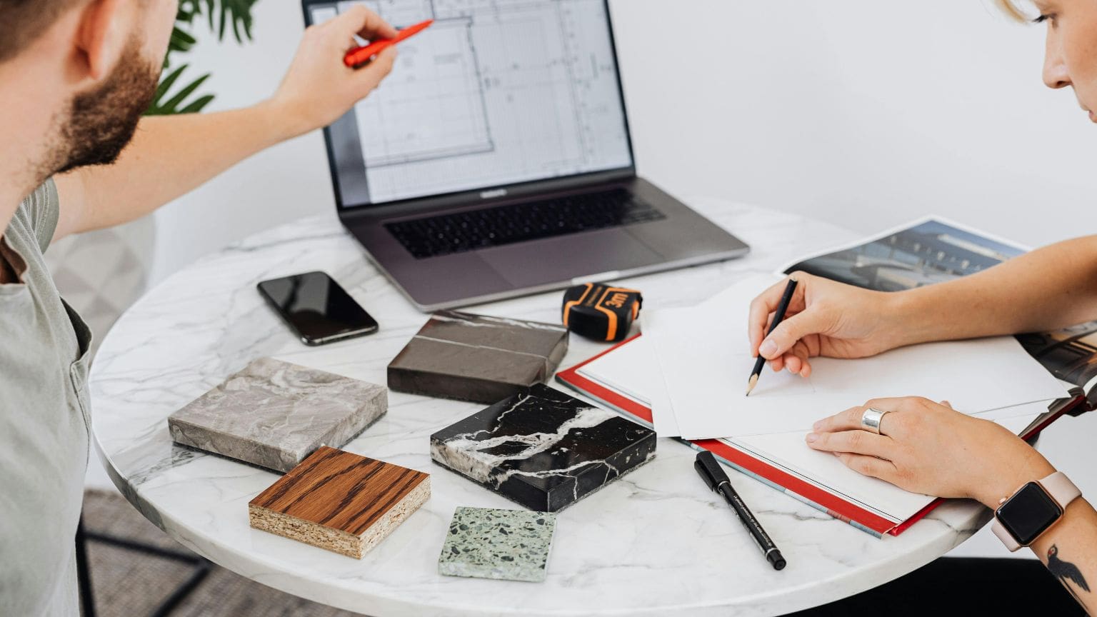 Selección de materiales y acabados para proyecto arquitectónico sobre mesa de trabajo, con planos y muestras visibles.