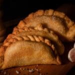 Empanadas argentinas caseras con masa dorada y repulgue artesanal servidas en mesa rústica junto a salsa criolla tradicional