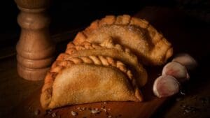Empanadas argentinas caseras con masa dorada y repulgue artesanal servidas en mesa rústica junto a salsa criolla tradicional