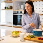 Persona cocinando en casa con ayuda de un curso online, comparado con grupo de personas aprendiendo cocina en un taller presencial.