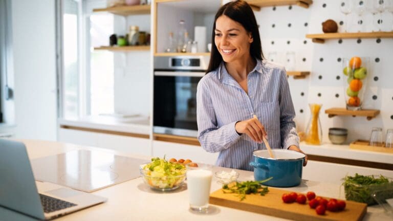 Persona cocinando en casa con ayuda de un curso online, comparado con grupo de personas aprendiendo cocina en un taller presencial.
