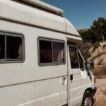 Caravana estacionada en Valencia bajo el sol, con signos de desgaste en pintura y techo, rodeada de clima seco y luz intensa.