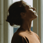 Mujer meditando en casa con luz natural, practicando mindfulness para la salud emocional.