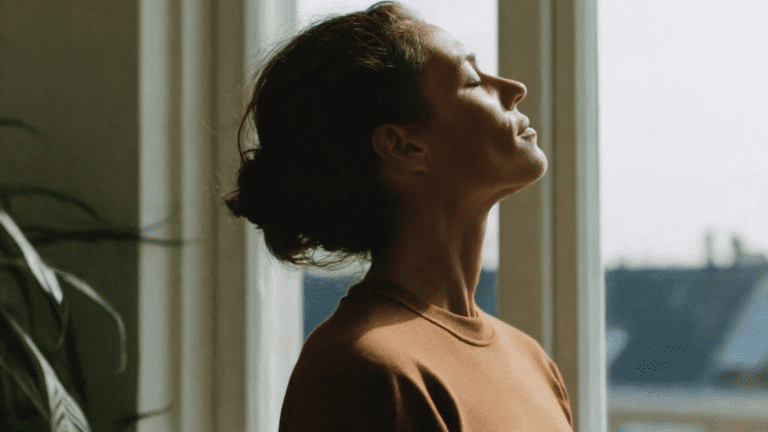 Mujer meditando en casa con luz natural, practicando mindfulness para la salud emocional.