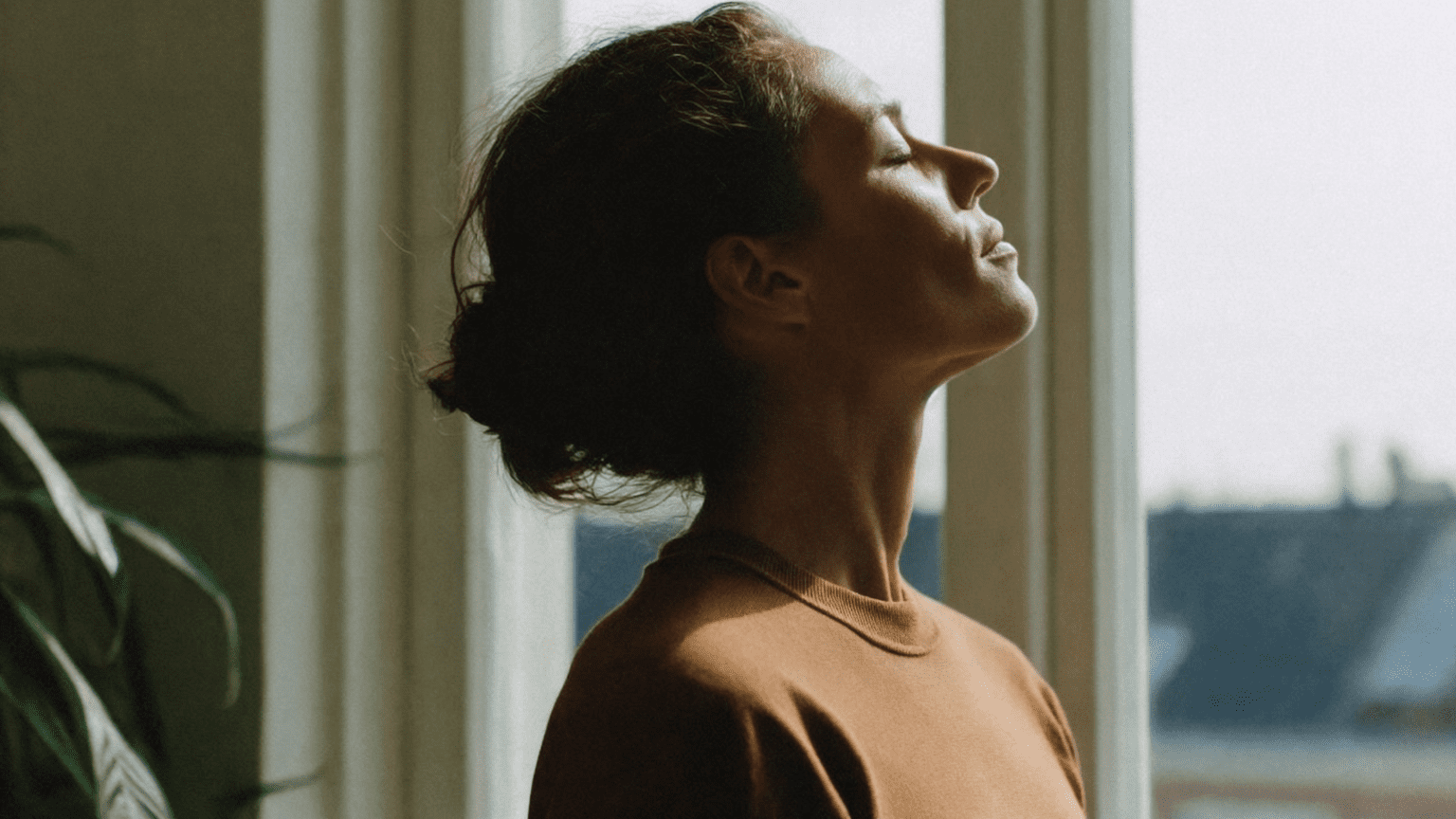 Mujer meditando en casa con luz natural, practicando mindfulness para la salud emocional.