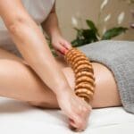 Mujer recibiendo maderoterapia corporal en centro de estética, masaje con rodillos de madera para reducir celulitis y mejorar la textura de la piel
