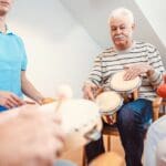 Personas mayores participando en una sesión de musicoterapia grupal, usando instrumentos sencillos y compartiendo una experiencia musical activa.