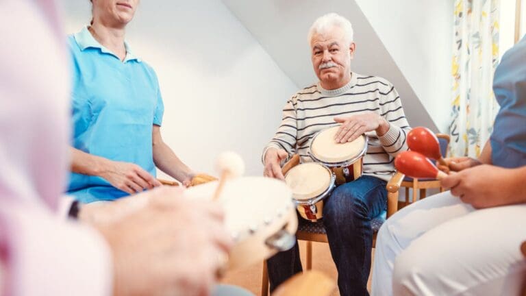 Personas mayores participando en una sesión de musicoterapia grupal, usando instrumentos sencillos y compartiendo una experiencia musical activa.