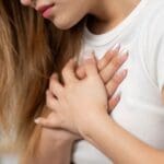 Mujer con expresión emocional tocándose el pecho, representación visual de los síntomas de la somatización y la conexión entre emociones y cuerpo.