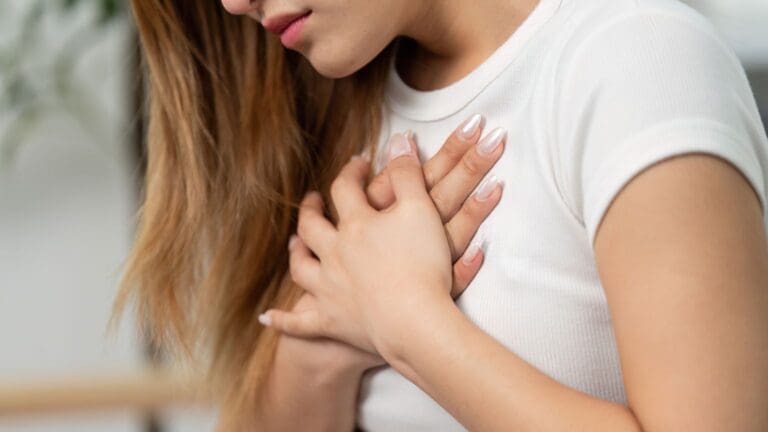Mujer con expresión emocional tocándose el pecho, representación visual de los síntomas de la somatización y la conexión entre emociones y cuerpo.