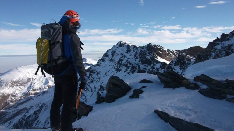 Turismo en Granada desde la alta montaña con montañista contemplando las cumbres nevadas de Sierra Nevada