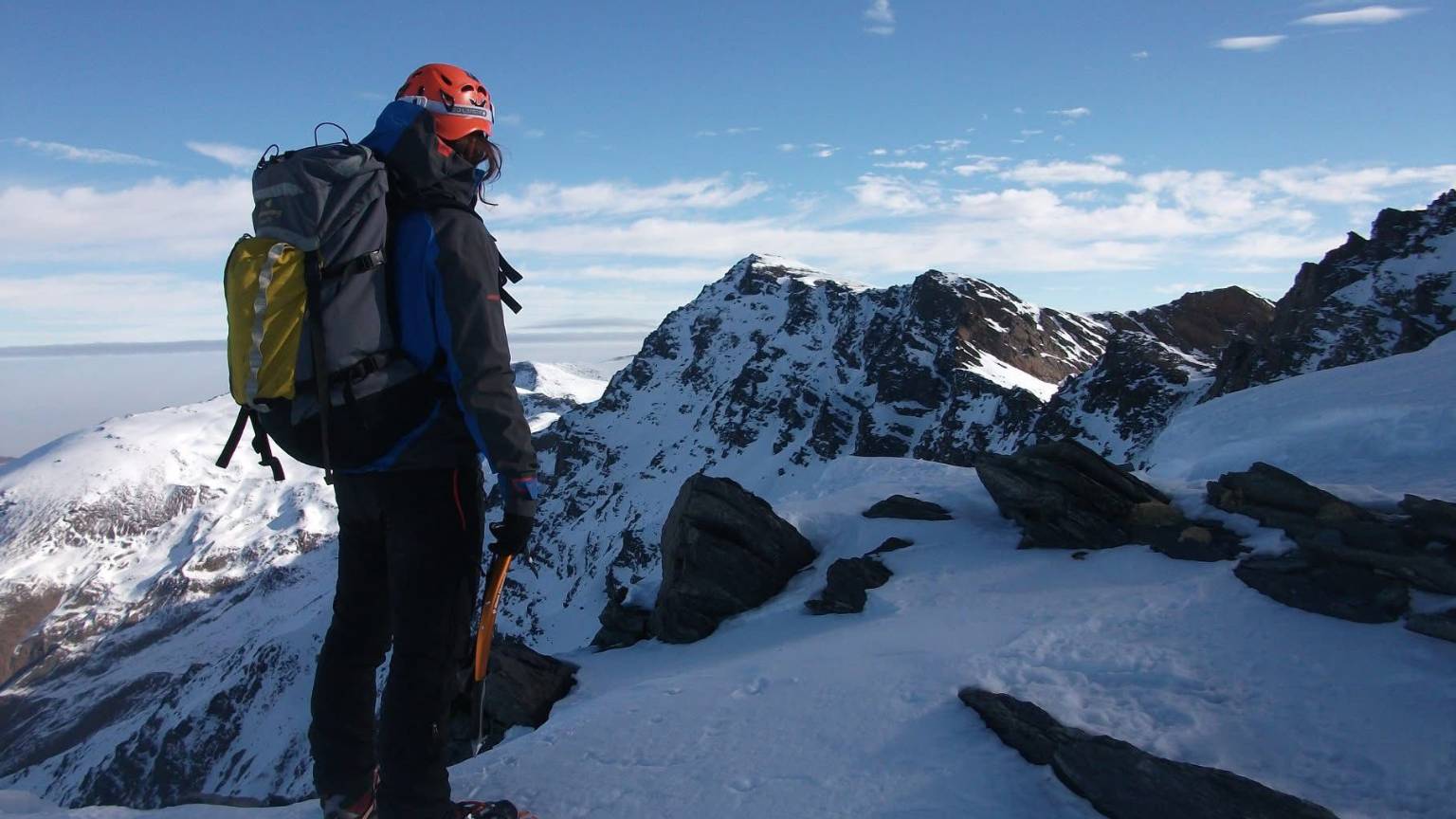 Turismo en Granada desde la alta montaña con montañista contemplando las cumbres nevadas de Sierra Nevada