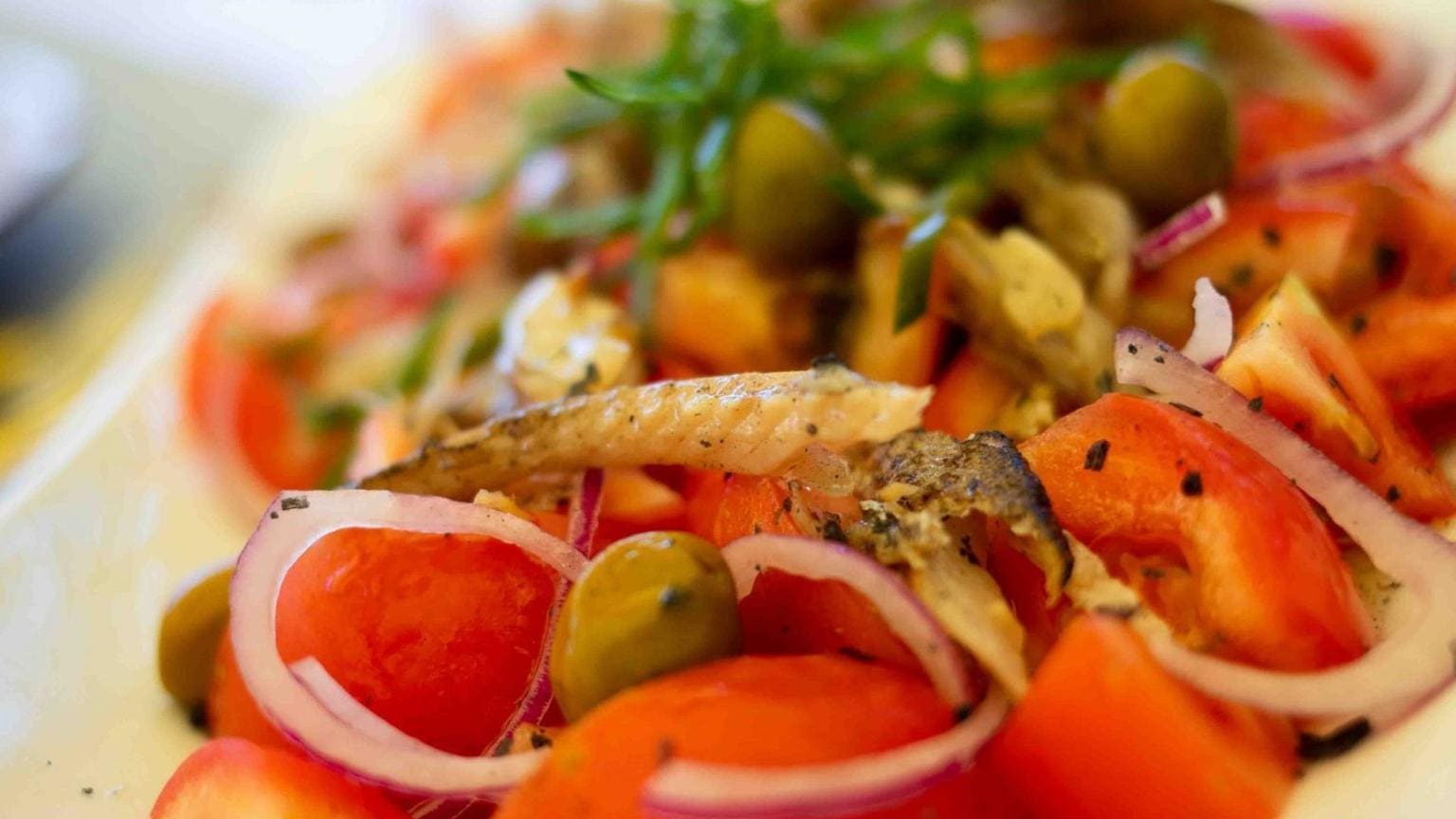 Ensalada fresca con tomate, aceitunas, cebolla morada y pescado típica de un restaurante mediterráneo tradicional